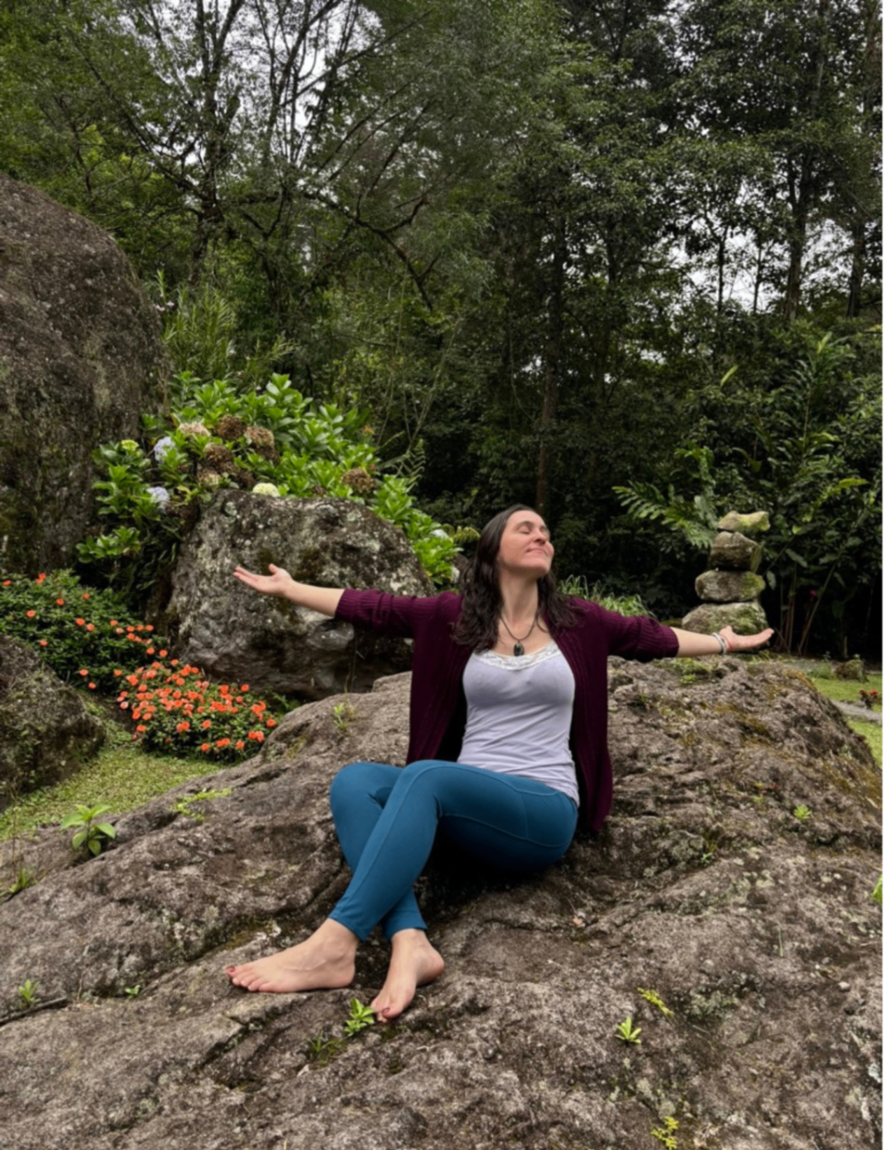 Christene sitting on a mossy stone in nature, arms open in receptive presence